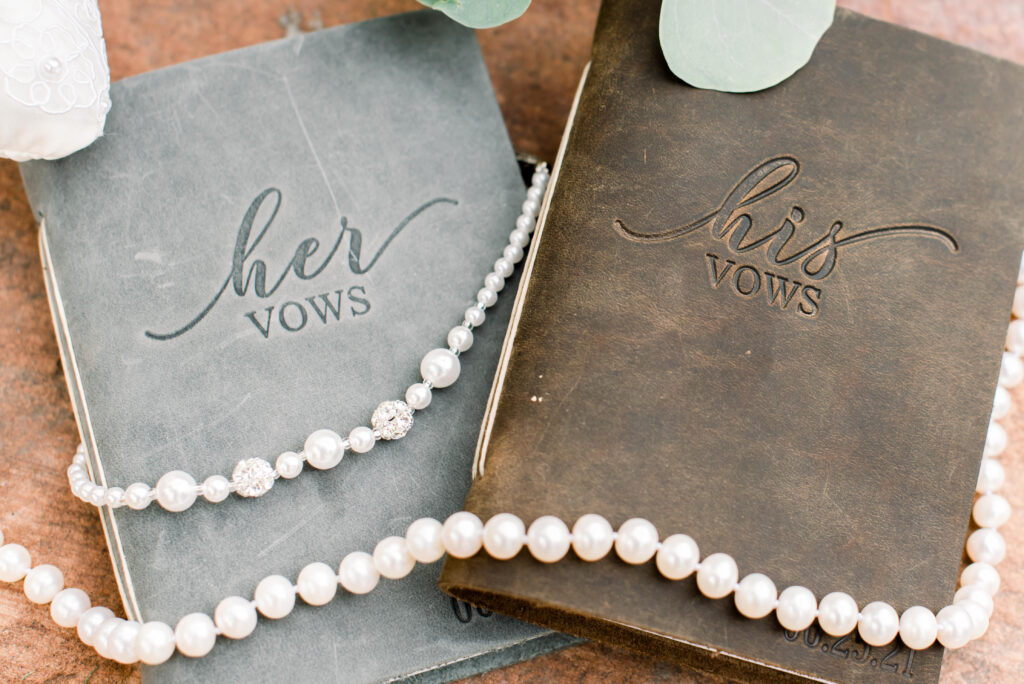Wedding detail photo of his and hers vow books with a pearl necklace